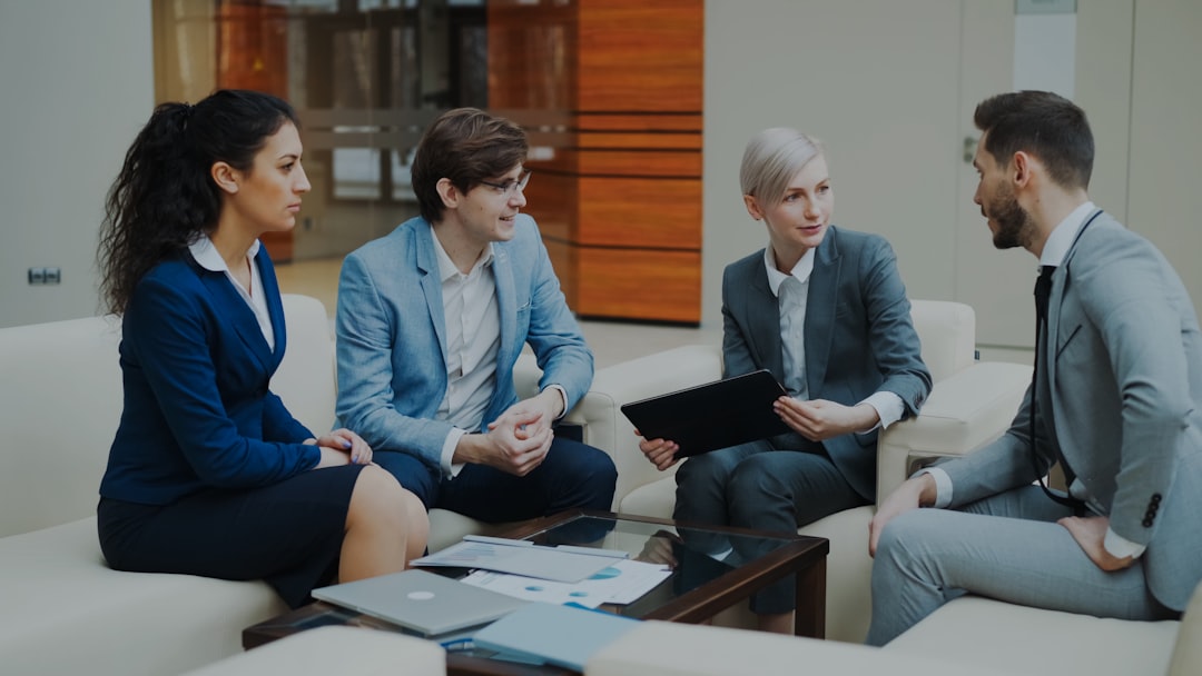 Businesswoman with digital tablet talking with male and female business colleagues sitting on couch in modern office indoors